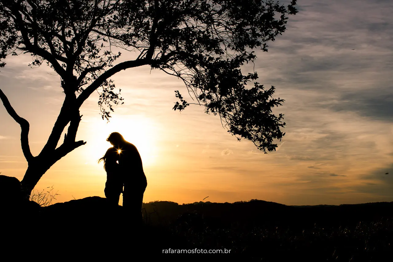 Casal em silhueta durante ensaio pré wedding nas montanhas com pôr do sol refletido na água